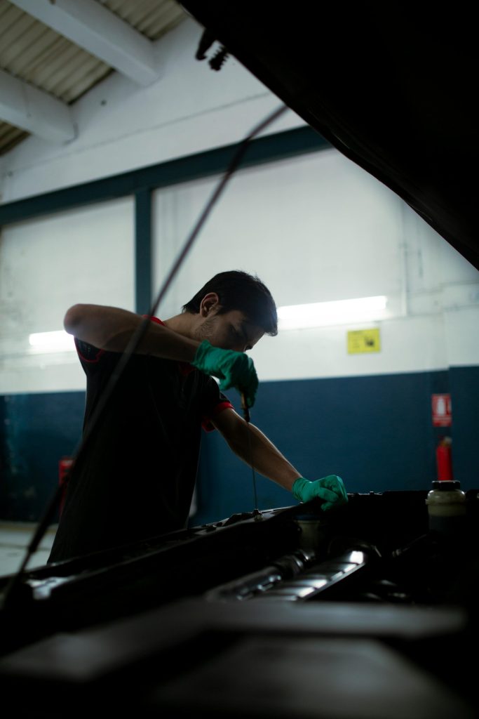 Mechanic checks engine oil in a car inside an auto garage, highlighting routine maintenance.